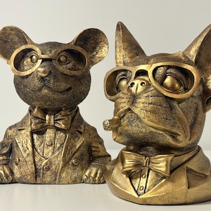 Könnte beinhalten: Zwei goldfarbene Kunstharzfiguren: eine Maus und eine Bulldogge. Beide tragen goldgerahmte Brillen und Fliegen. Die Bulldogge hat eine Zigarre im Mund. Maus und Bulldogge tragen Anzüge.