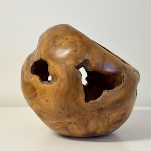 Könnte beinhalten: Eine handgefertigte Holzschale mit einer einzigartigen, organischen Form. Die Schale besteht aus hellbraunem Holz und weist mehrere unregelmäßige Öffnungen auf. Die Holzmaserung ist sichtbar und trägt zur natürlichen Ästhetik bei. Diese dekorative Schale eignet sich für die Inneneinrichtung.