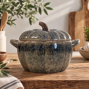 Peut inclure: Une cocotte en céramique en forme de citrouille avec un couvercle, dotée d'un vernis tacheté bleu et marron. Le récipient présente un extérieur nervuré, deux poignées latérales et une petite poignée en forme de tige sur le couvercle.
