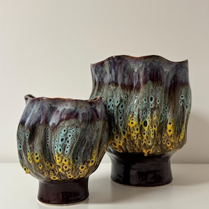 Può includere: Due vasi in ceramica con una glassa strutturata unica. I vasi presentano una base marrone scuro e una parte superiore increspata con una miscela di colori, tra cui giallo, verde acqua e viola intenso. Il vaso più grande è alto circa 25 cm.