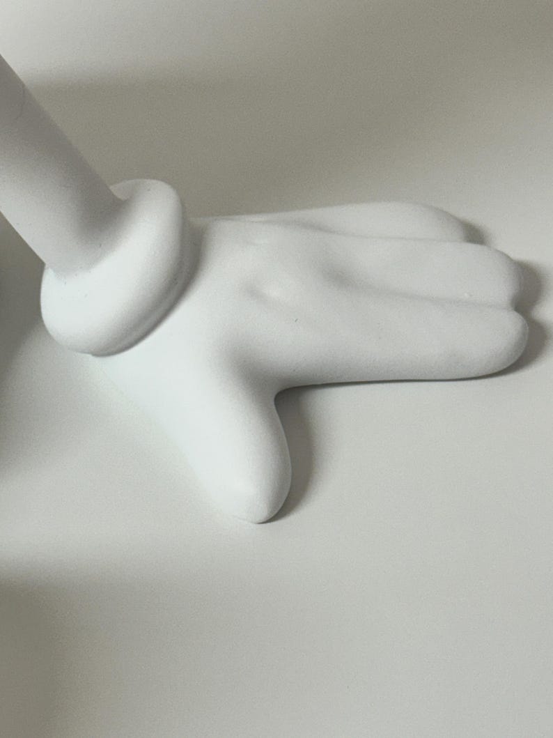 Pu&ograve; includere: Una scultura di mano bianca stilizzata con un polso arrotondato e un dettaglio ad anello. Le dita sono leggermente curve e il design generale &egrave; liscio e minimalista. La scultura &egrave; ambientata su uno sfondo bianco.