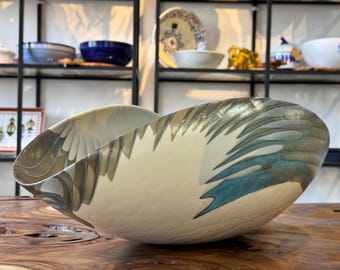 May include: A large, white ceramic bowl with a unique, abstract design featuring blue, brown, and gold accents. The bowl has a slightly curved shape and a smooth, glossy finish.