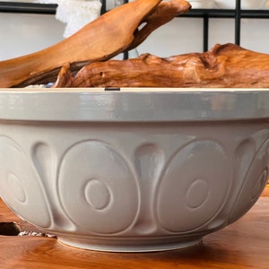 May include: A large, gray ceramic mixing bowl with a fluted design. The bowl is empty and sitting on a wooden surface.