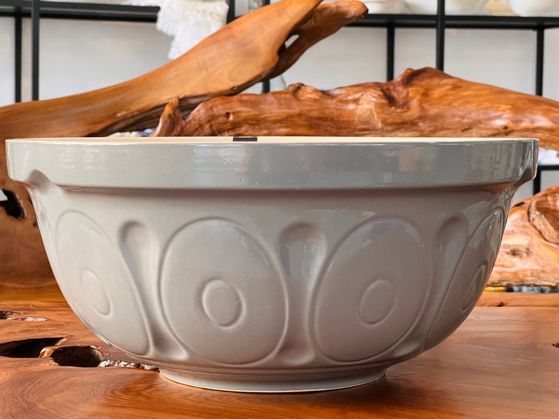 May include: A large, gray ceramic mixing bowl with a fluted design. The bowl is empty and sitting on a wooden surface.