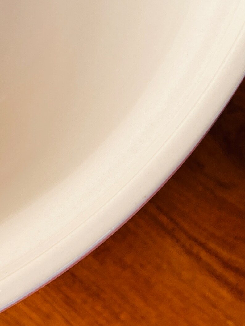 May include: Close-up of the bottom edge of a white ceramic bowl. The bowl has a smooth, rounded edge and a slight lip.