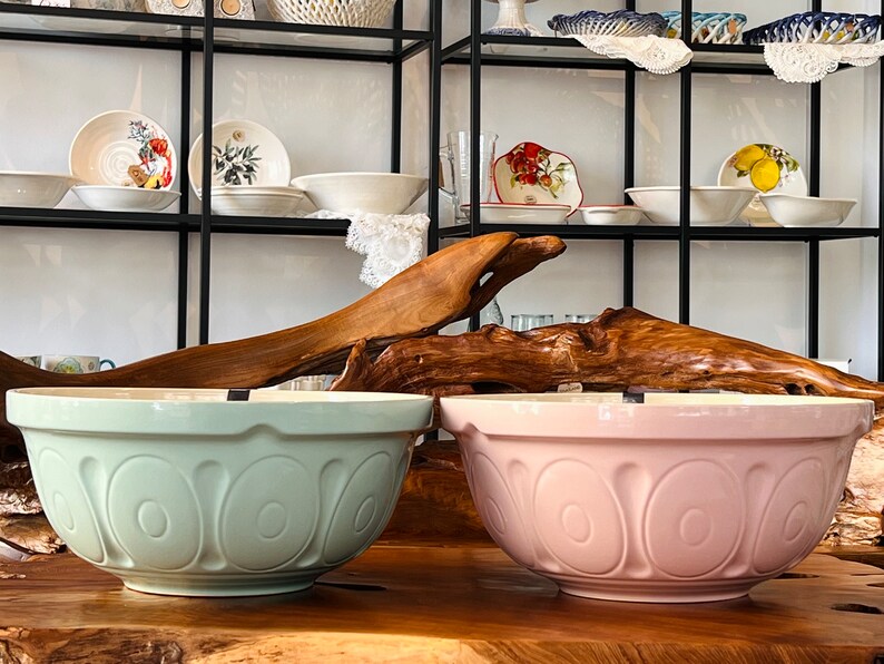 May include: Two large ceramic mixing bowls, one in a light green color and one in a light pink color. Both bowls have a decorative pattern of raised ovals around the rim.