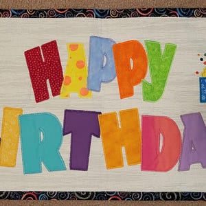 May include: A white banner with the words "Happy Birthday" in colorful letters. The banner is decorated with balloons, a cake, and presents.