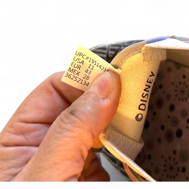 May include: Close-up of a shoe's interior, featuring a tag with size information: USA 11, EUR 43, and MEX 28. The shoe's lining has a floral pattern. The word "DISNEY" is printed on the shoe's interior.