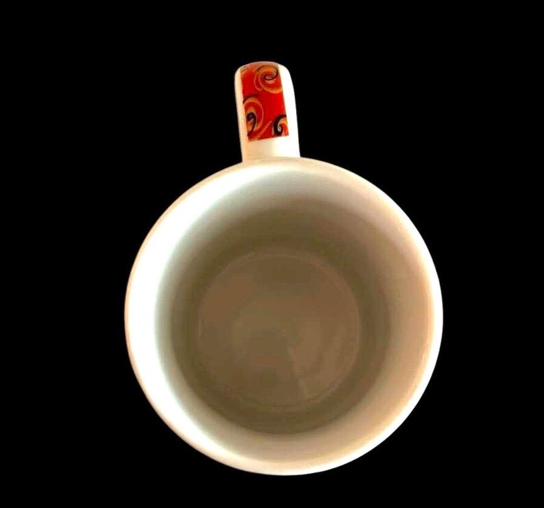 May include: White ceramic coffee mug with a red, orange and yellow patterned handle.