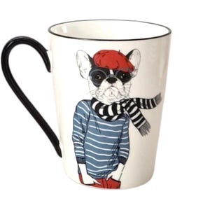 May include: White ceramic mug with a black handle and rim. The mug features a cartoon illustration of a French bulldog wearing a red beret, glasses, and a striped scarf. The dog is also wearing a blue striped shirt and red pants.