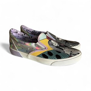 May include: Pair of slip-on sneakers featuring a colorful design inspired by a movie. The shoes have a white sole, a yellow and teal upper, and a black and white striped design on the toe. The heel is clear with a holographic effect.