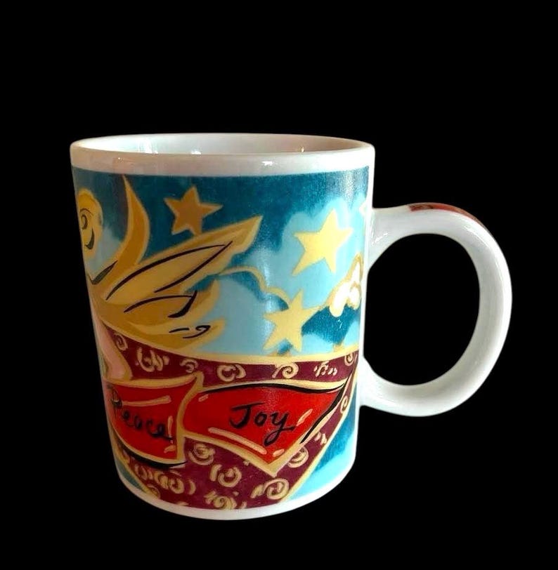 May include: White ceramic mug with a blue, teal, and gold design featuring a flying angel with a banner that reads "Peaceful Joy".