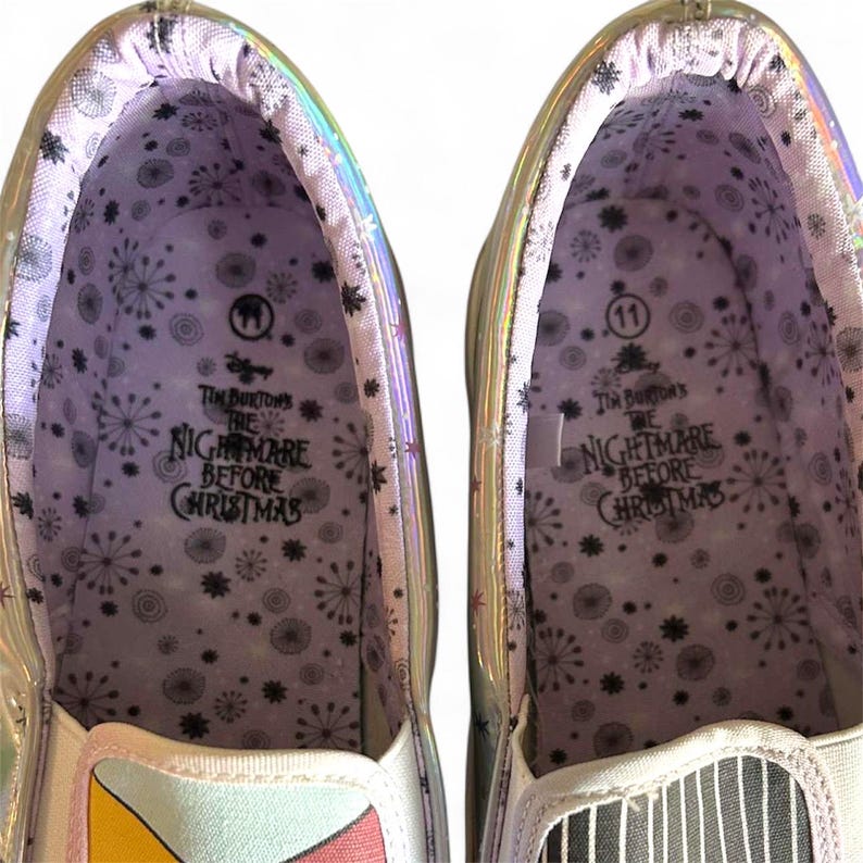 May include: Pair of slip-on shoes with iridescent trim. The interior features a snowflake pattern and the text "Tim Burton's The Nightmare Before Christmas." One shoe is size 11.
