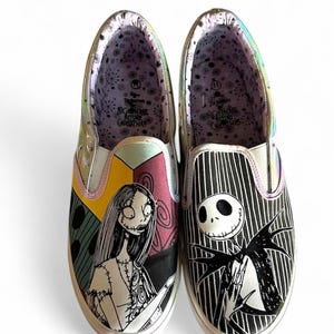 May include: Pair of slip-on shoes featuring characters from The Nightmare Before Christmas. One shoe displays Sally, the other Jack Skellington. The shoes have a white sole, and the interior lining has a patterned design with the movie title.