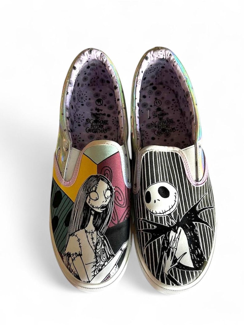 May include: Pair of slip-on shoes featuring characters from The Nightmare Before Christmas. One shoe displays Sally, the other Jack Skellington. The shoes have a white sole, and the interior lining has a patterned design with the movie title.