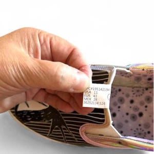 May include: Close-up of a shoe's interior, showcasing a label with size information: USA 11, EUR 43, and MEX 28. The shoe features a black and white design on the outer sole and a colorful, iridescent material on the inner lining.