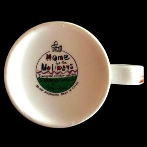 May include: White ceramic mug featuring a green, red, and purple Christmas bauble design. The bauble reads "Home for the Holidays" and is designed exclusively for Starbucks Coffee Co. by Mary Jane.