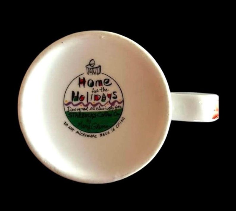 May include: White ceramic mug featuring a green, red, and purple Christmas bauble design. The bauble reads "Home for the Holidays" and is designed exclusively for Starbucks Coffee Co. by Mary Jane.
