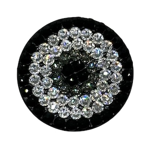 May include: A black round phone grip with a circle of clear rhinestones around a center of black and gray rhinestones.