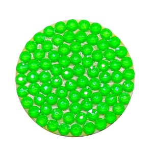 May include: A round, decorative object with a light beige border and a vibrant green, gem-like surface. The surface is covered with numerous, small, faceted, bright green gems, creating a sparkling effect. The object is set against a plain white background.