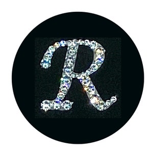 May include: A silver letter R made of rhinestones on a black background.