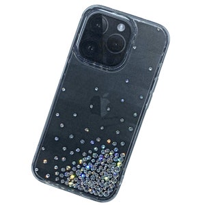 May include: A clear phone case with a black phone inside. The case is decorated with iridescent rhinestones that are scattered across the back of the case.