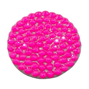 May include: A round, pink, sparkly embellishment with a flat back. The embellishment is made of small, round rhinestones.