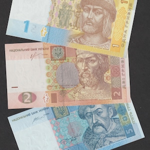 Puede incluir: Tres billetes ucranianos: un billete de 1, 2 y 5 grivnas. Los billetes presentan retratos de figuras históricas y el escudo de armas ucraniano. Los billetes son en tonos de azul, rosa y amarillo.