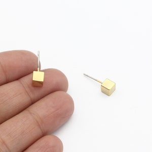 May include: A pair of gold cube stud earrings. The earrings are small and simple, and they would be a great addition to any jewelry collection.