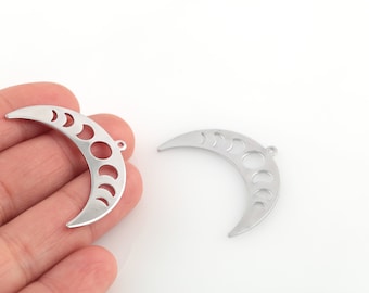 May include: Two silver-colored crescent moon charms with phases cut out. Each charm has a small loop at the top for attaching to jewelry. The charms are on a white background.