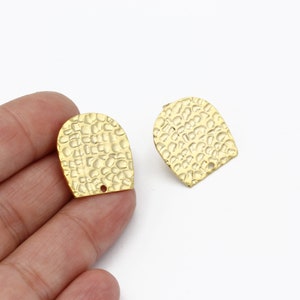 May include: Two gold-toned metal charms with a textured surface in the shape of a rounded rectangle with a hole at the top.