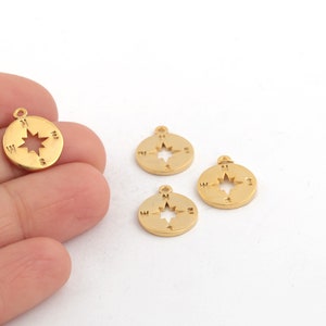 May include: Four gold-colored compass charms with a star design and the letters N, S, E, and W. The charms are on a white surface.