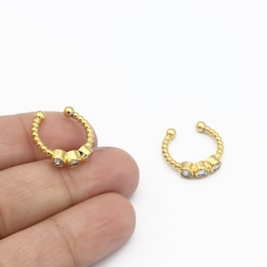 May include: Two gold nose rings with three clear rhinestones each. The rings are open and have a beaded design.
