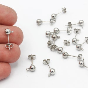 May include: A close-up of a silver earring finding with a round ball at the end. There are multiple earring findings scattered on a white surface.