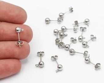 May include: A close-up of a silver earring finding with a round ball at the end. There are multiple earring findings scattered on a white surface.