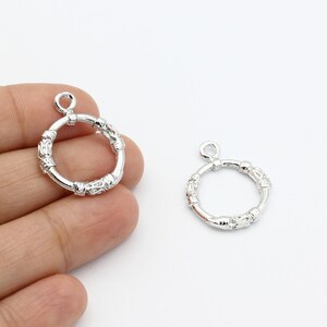 May include: Two silver-toned metal circle charms with a textured design. Each charm has a loop at the top for attaching to jewelry or other crafts.