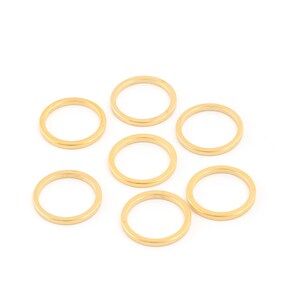 May include: Seven gold-colored metal rings, all the same size, are scattered on a white background.