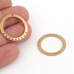 May include: Two gold-colored metal rings with small holes around the outer edge. The rings are about 1 inch in diameter.