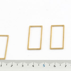 以下が含まれることがあります： 3つの異なるサイズの金色の金属製の長方形のフレーム。フレームは白い表面に置かれ、その下に定規があります。定規はセンチメートルでマークされています。