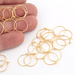 May include: A collection of small, gold-colored hoop earring findings. The open hoops are round and have a small loop at the bottom for attaching a charm or other embellishment. The findings are on a white background.