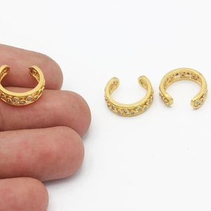 May include: Three gold ear cuffs with small clear stones set in the metal. The cuffs are open and have a curved shape.