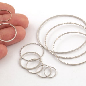 Op de afbeelding: Een set zilverkleurige metalen ringen in verschillende maten. De ringen zijn allemaal glad en hebben een licht getextureerd oppervlak.