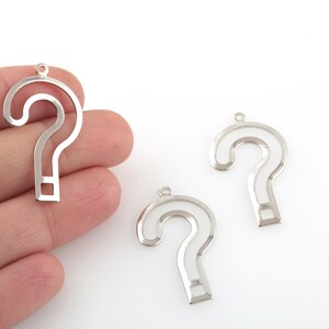 May include: Three silver question mark charms with a cutout design. The charms are made of metal and have a shiny finish.