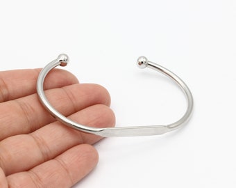 May include: A silver bangle bracelet with rounded ends. The bracelet is open and has a flat, rectangular section in the middle.