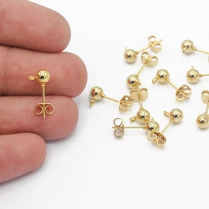 May include: A close-up of gold-toned earring findings with a round ball at the top. The findings are on a white surface.