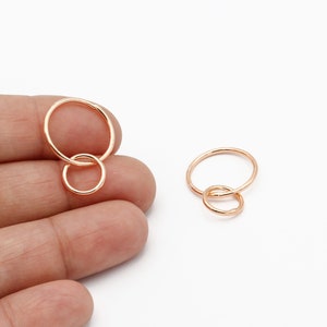 May include: Two rose gold-colored hoop earrings, one large and one small, interlocked. The earrings are displayed on a white background. The smaller hoop is connected to the larger hoop. The earrings are a jewelry item.