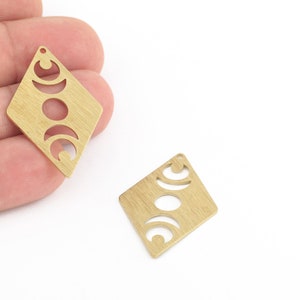 May include: Two gold-colored metal charms in the shape of a diamond with a cut-out design of three crescent moons.