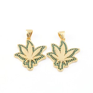 Puede incluir: Dos colgantes de tono dorado en forma de hoja de marihuana con detalles de esmalte verde.