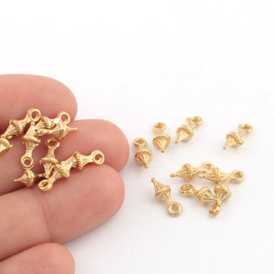 May include: A group of gold-toned metal charms with a decorative, textured design. The charms have a loop on one end and a pointed, cone-shaped design on the other end.