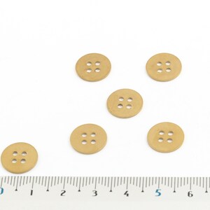 May include: Six beige wooden buttons with four holes each, arranged in a semi-circle on a white surface with a ruler for scale.
